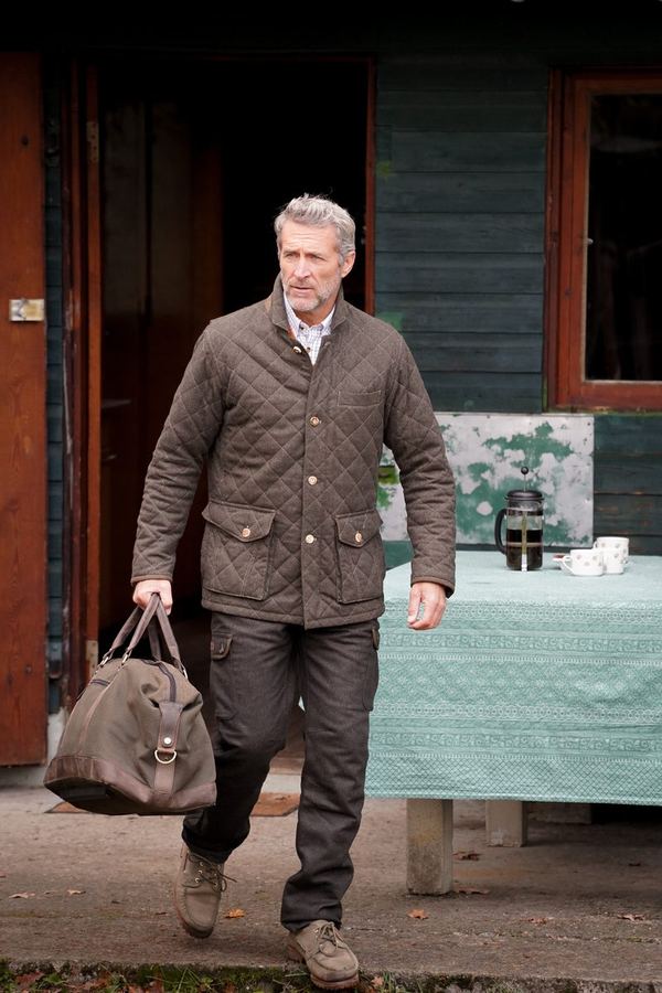 A man wearing a quilted Rascher Jakko jacket carrying a travel bag